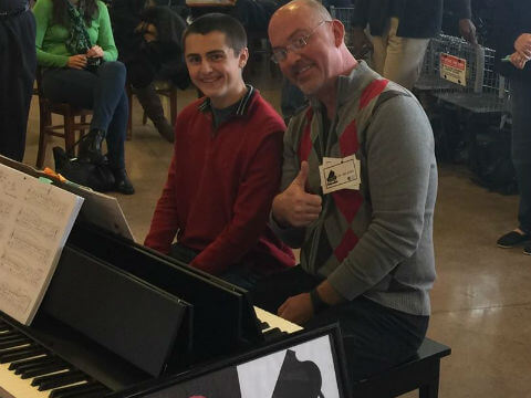a conservatory teacher sitting next to a student at a christmas concert while playing the piano