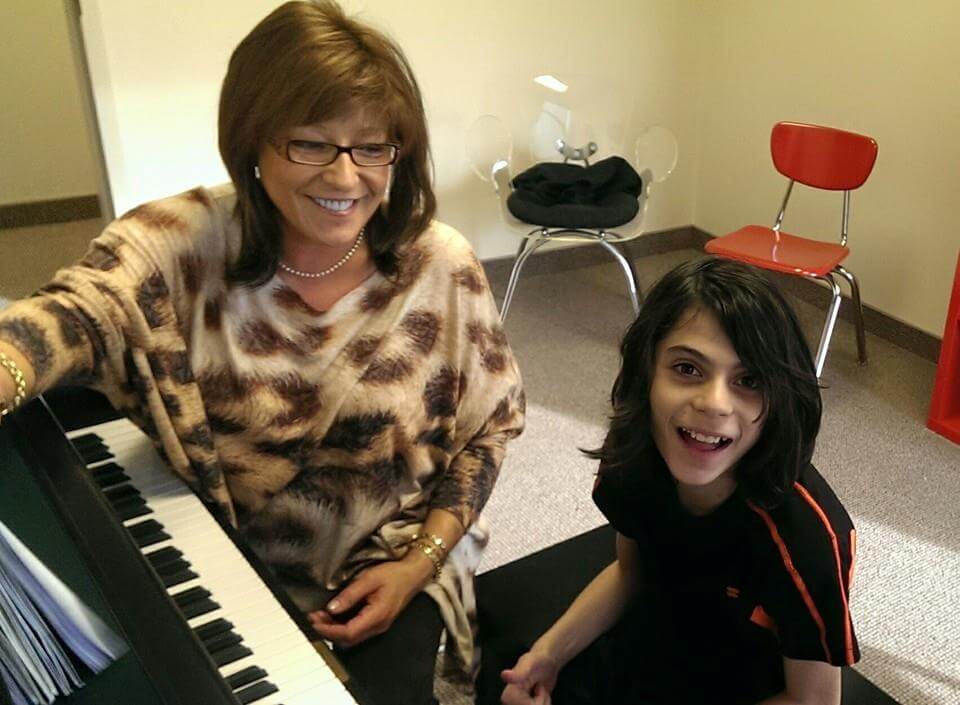 A young male student sitting next to his piano teacher at the piano, smiling at the camera