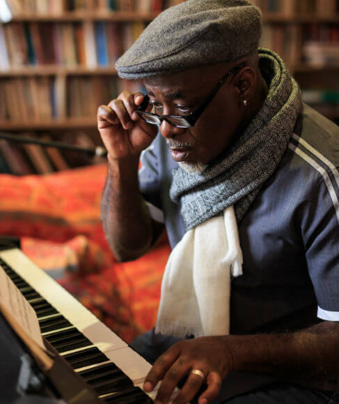 A man in a hat and glasses playing a piano in his living room
