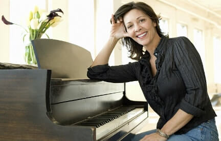 A woman smiling and leaning on her piano