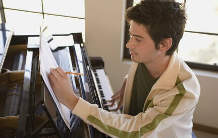 A young man sitting at a piano composing his own sheet music.