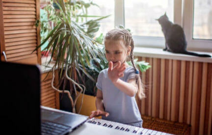 You girl playing piano and waving at her teacher via zoom