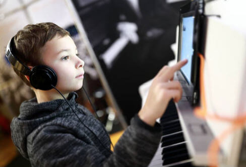 a young boy playing the piano while interacting on Zoom for piano lessons