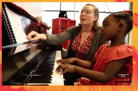 A teacher and her student playing piano together