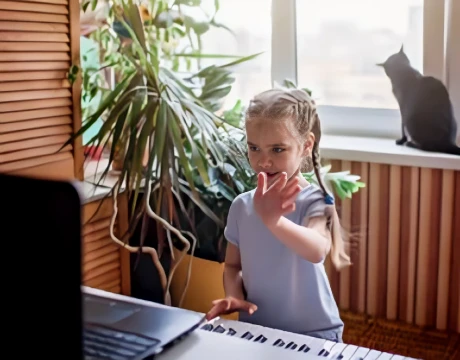 girl waving to her piano teacher on a laptop